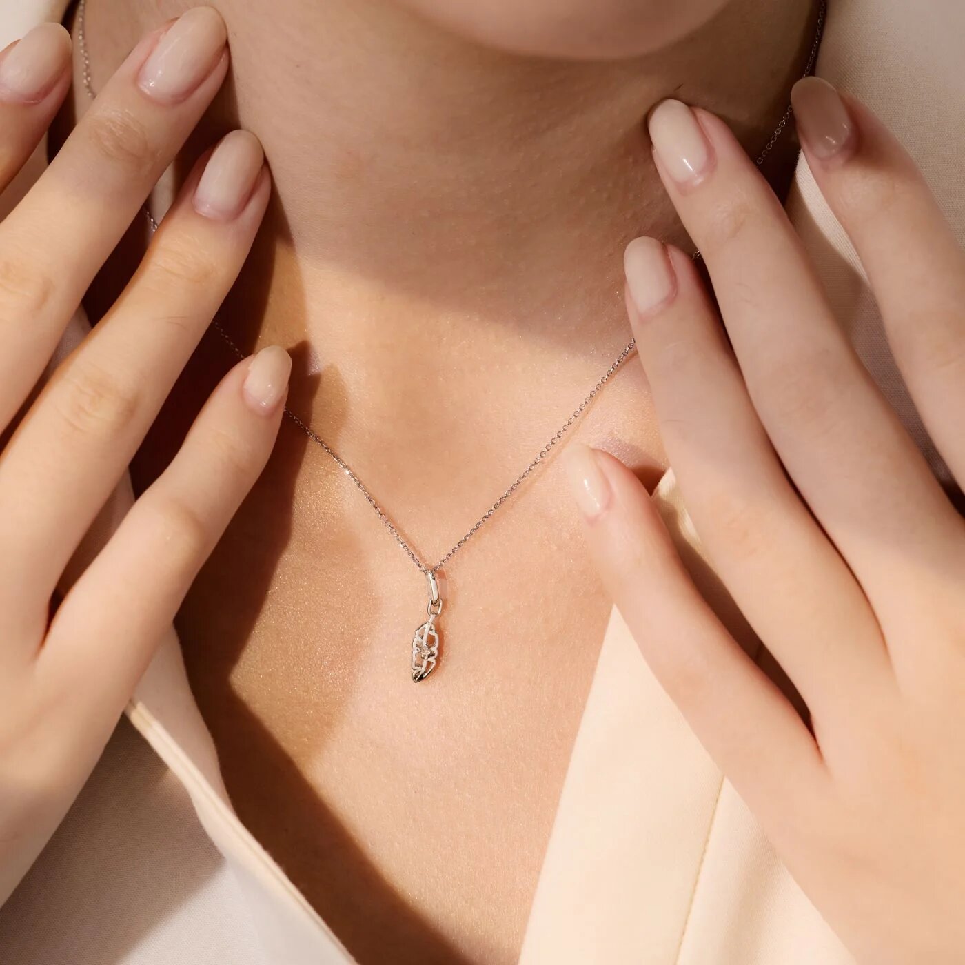Close-up of a woman adjusting a thin silver necklace with a small pendant at the base of her neck.