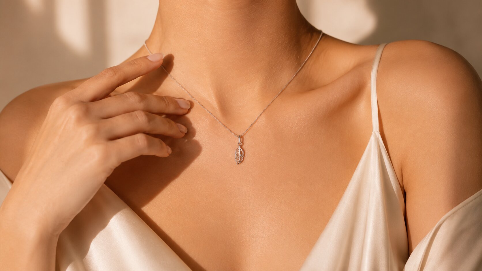 Woman wearing a delicate silver pendant necklace with an ivory satin top.