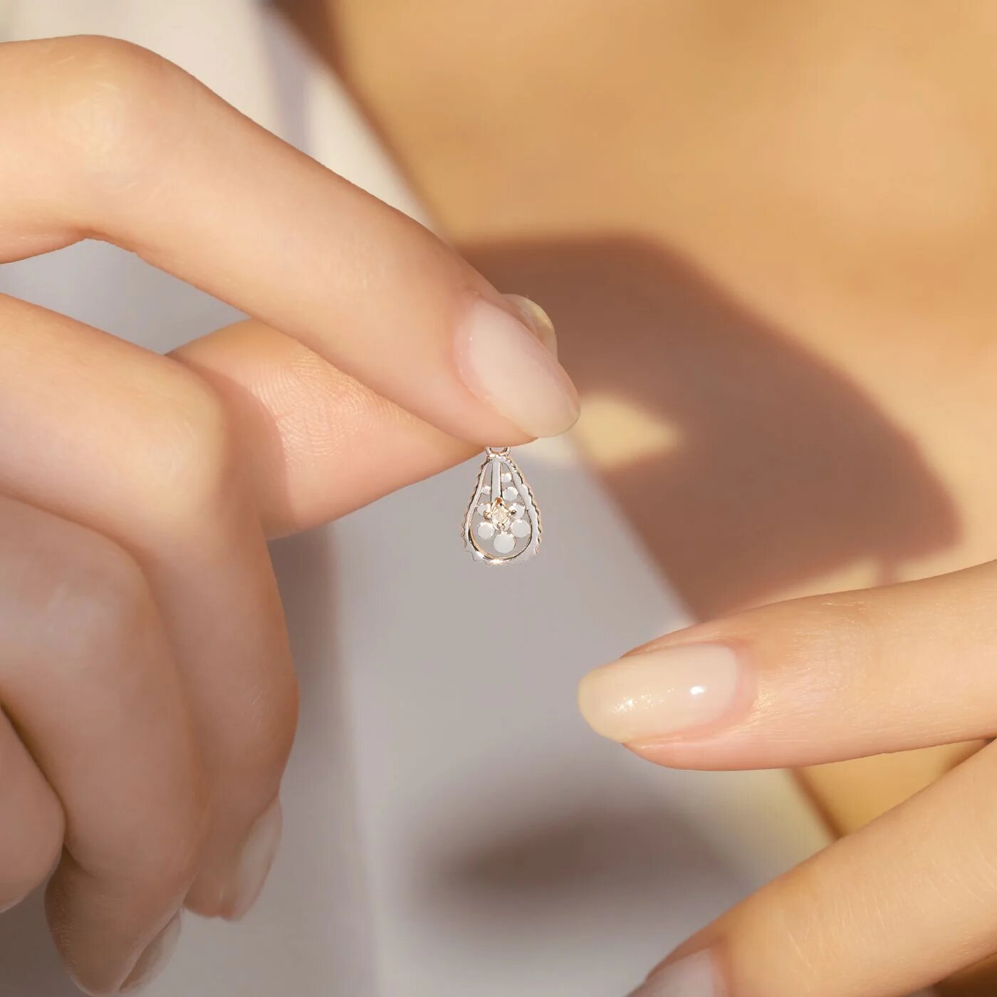 Close-up of hands holding a delicate teardrop pendant with a small floral design, symbolizing love and emotional harmony